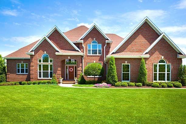 A large brick house with a lush green lawn in front of it.