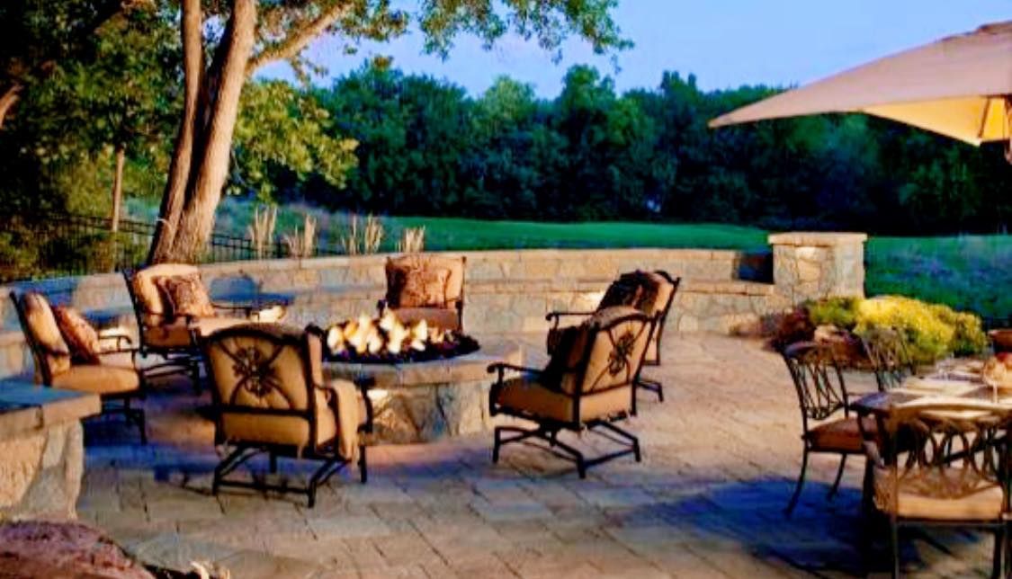 A patio with a fire pit , chairs , tables and umbrellas.