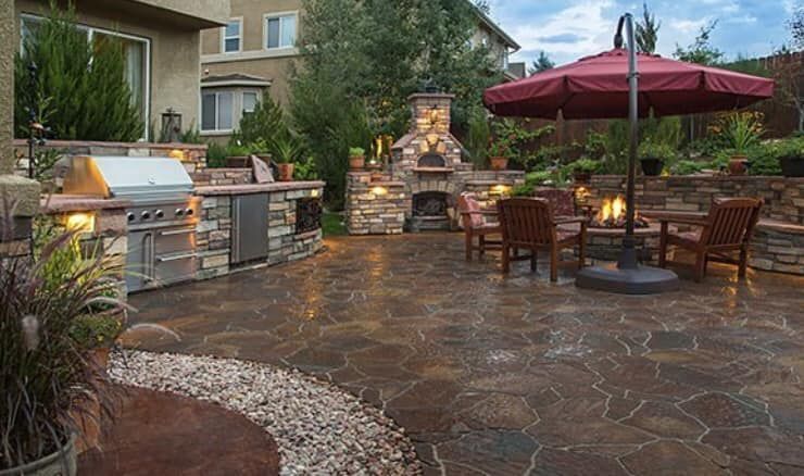 A patio with a grill , umbrella , chairs and a fireplace.
