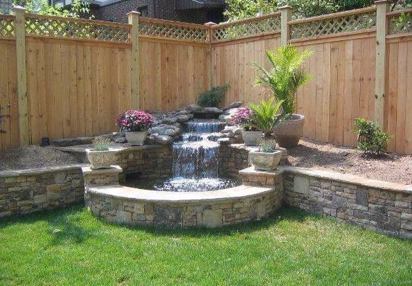 A waterfall is surrounded by a wooden fence in a backyard.