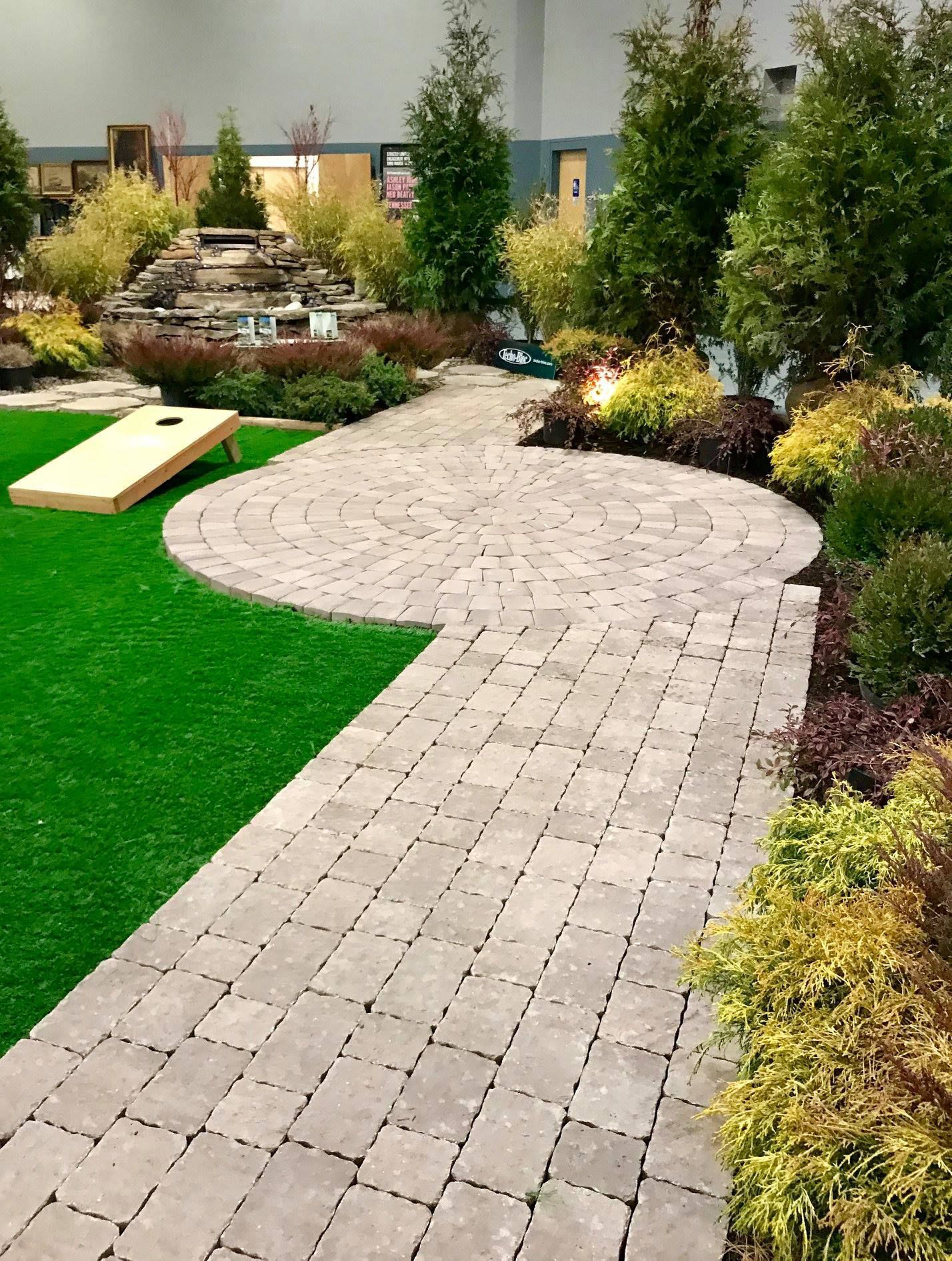 A brick walkway leading to a lush green yard with a cornhole board.