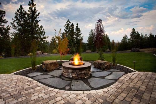 A fire pit in the middle of a patio with trees in the background.