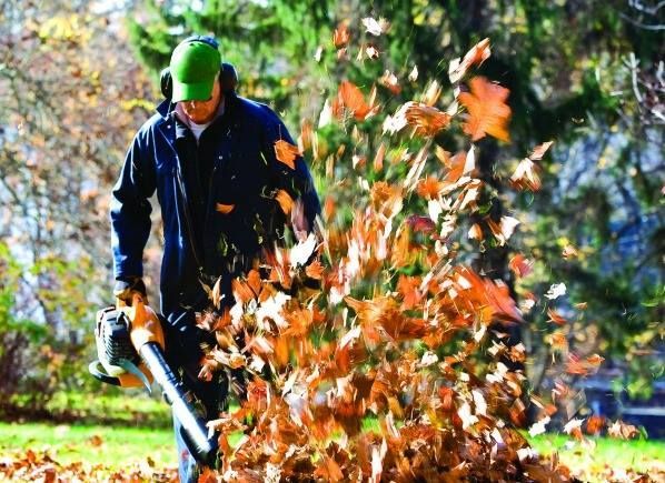 A man is blowing leaves with a leaf blower.