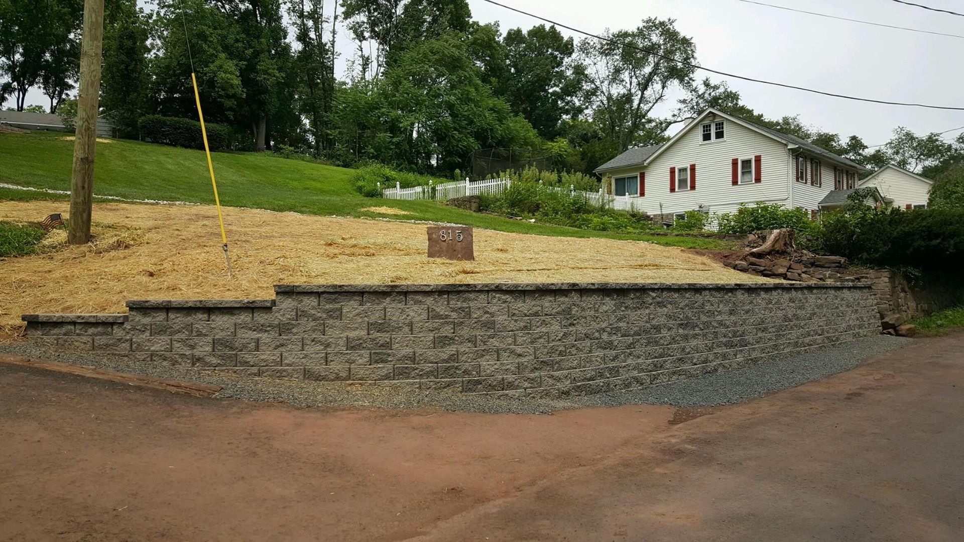 A stone wall is sitting on the side of a road next to a house.