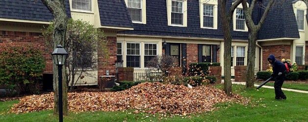 A man is raking leaves in front of a house.