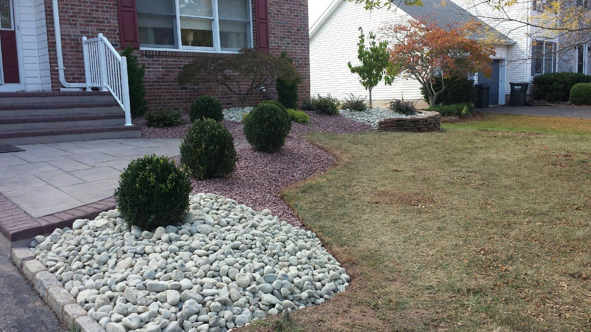 A house with a lush green lawn and a rock garden in front of it.