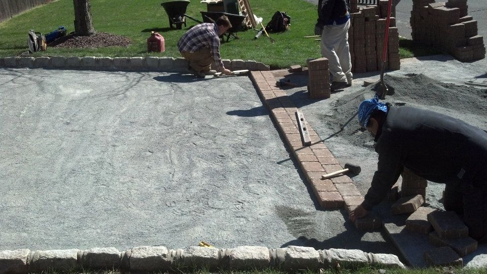 A group of men are working on a brick driveway