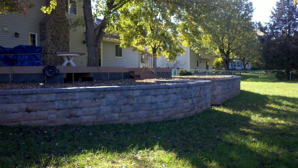 A brick wall surrounds a lush green lawn in front of a house.