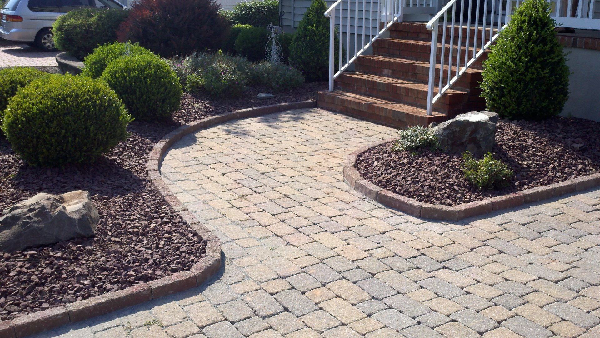A brick walkway leading to a house with stairs and bushes