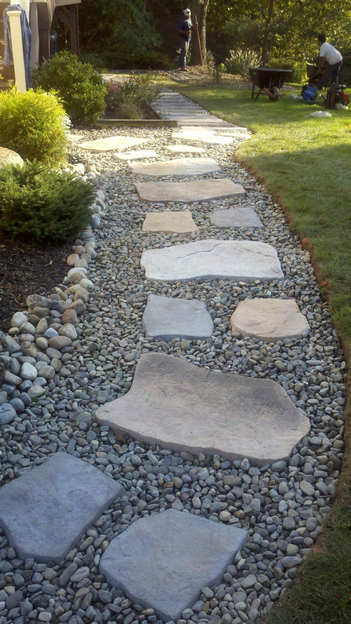 A stone walkway in a backyard surrounded by rocks and grass.