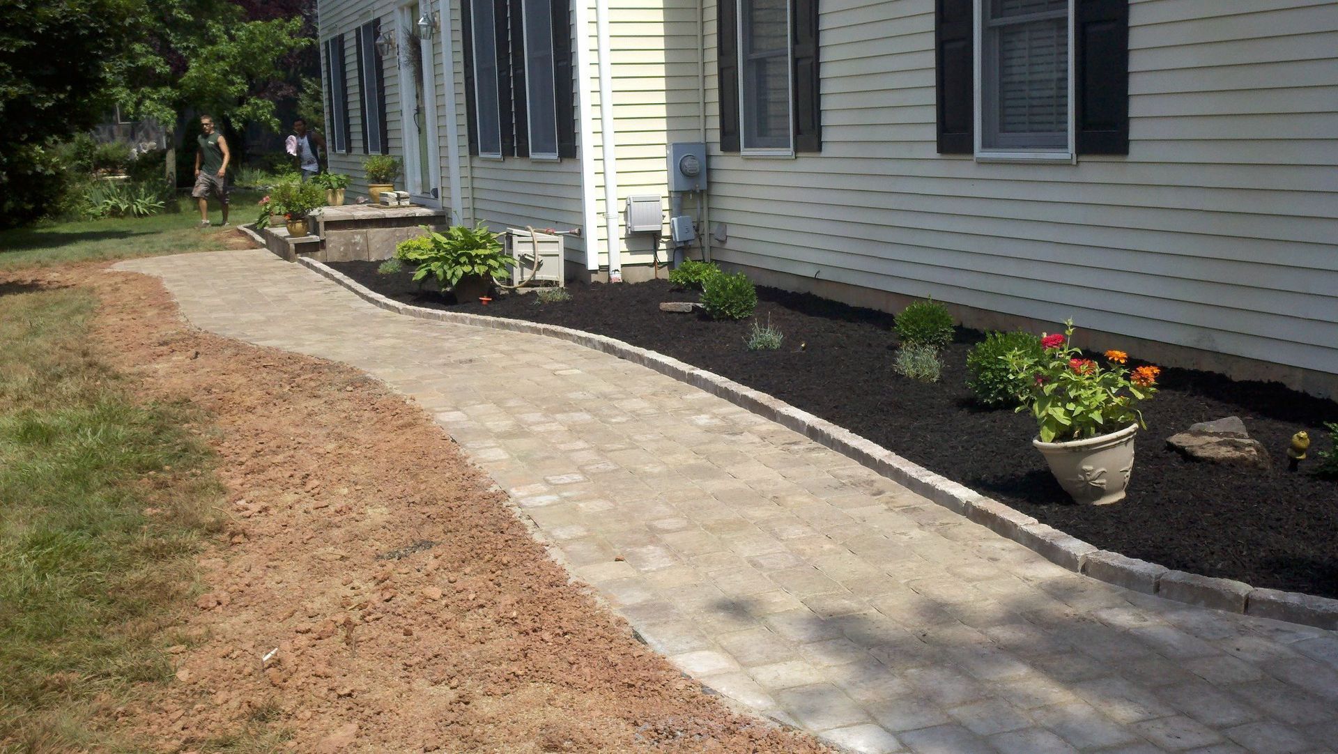 A brick walkway leading to a white house with black shutters