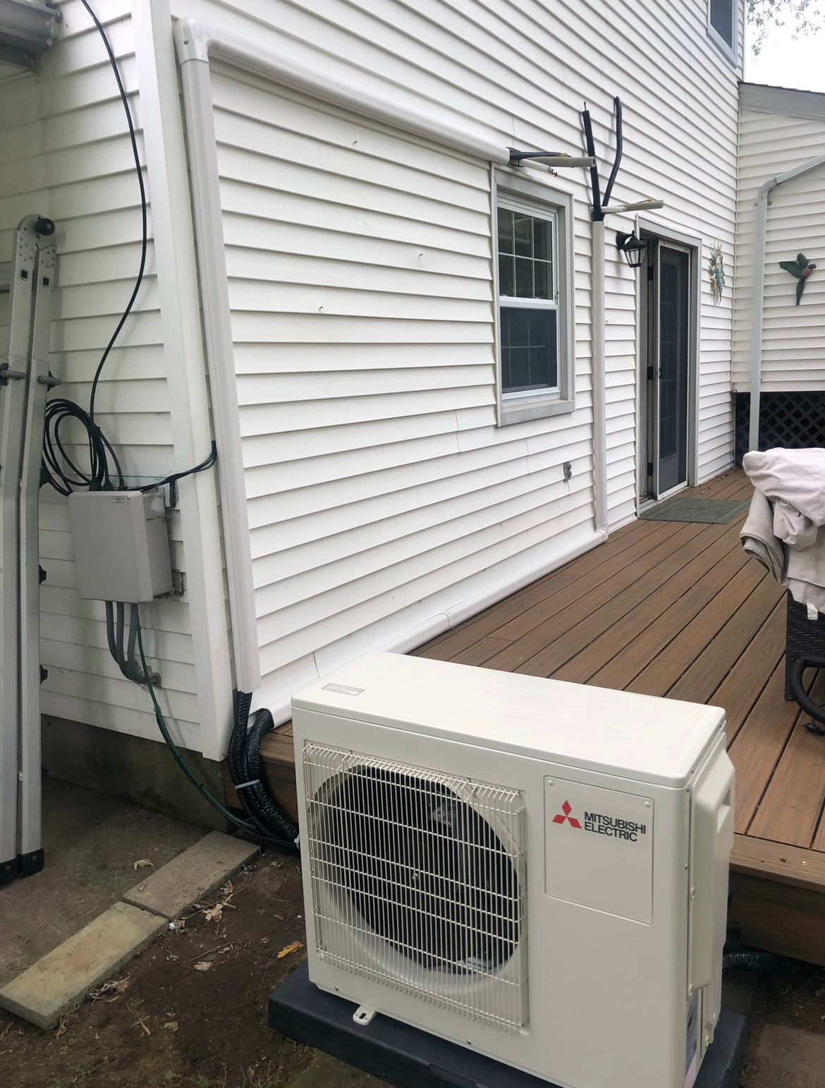 A white air conditioner is sitting on a wooden deck next to a white house.
