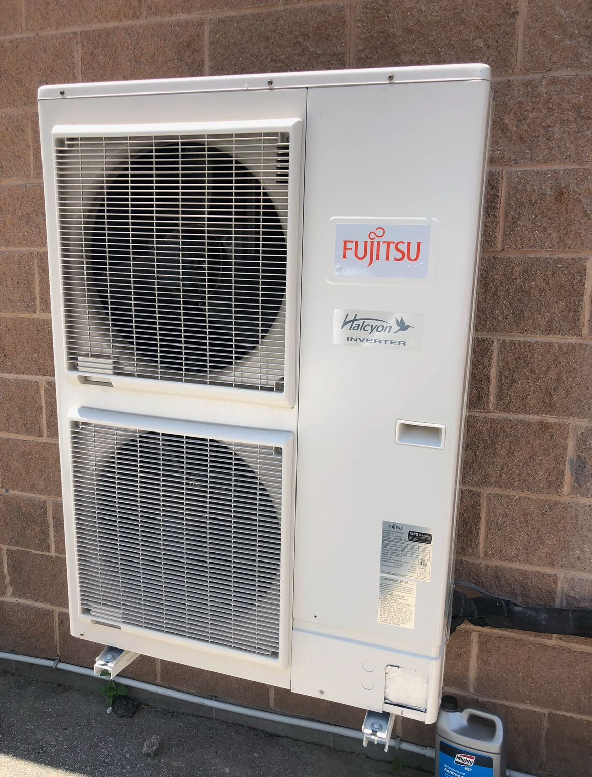 A fujitsu air conditioner is mounted on a brick wall.