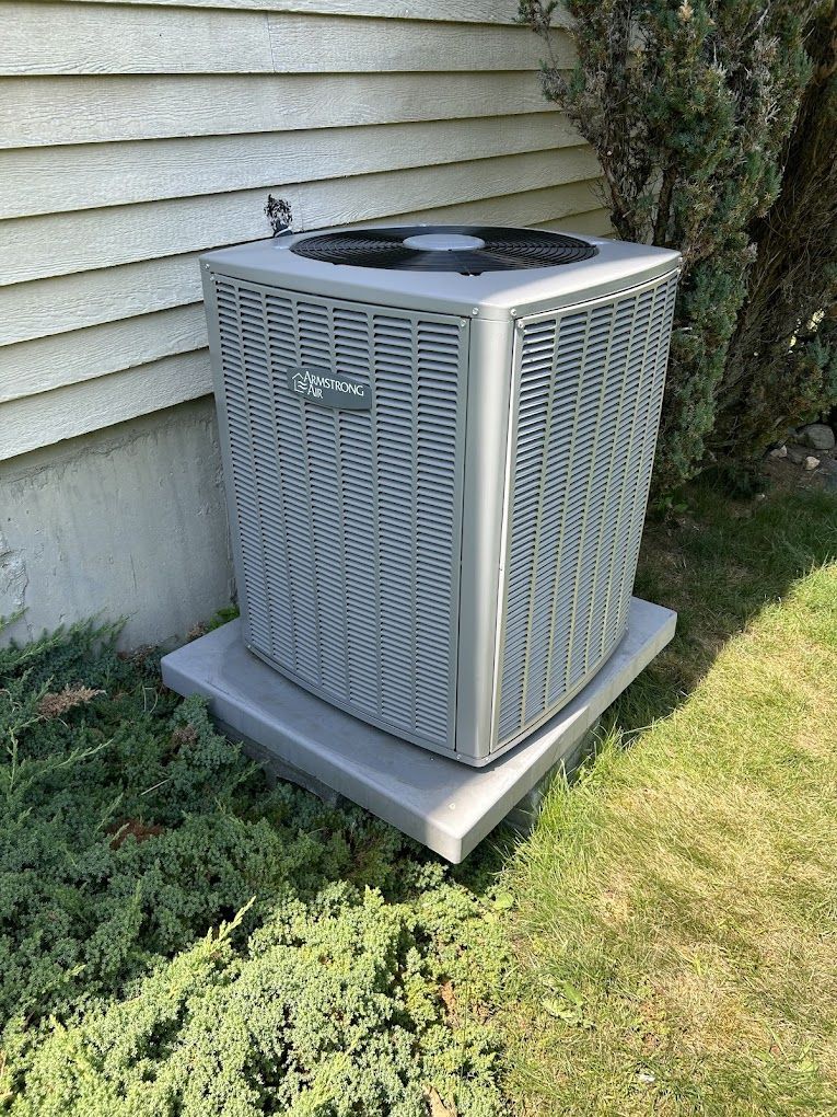 A large air conditioner is sitting on top of a concrete base in front of a house.