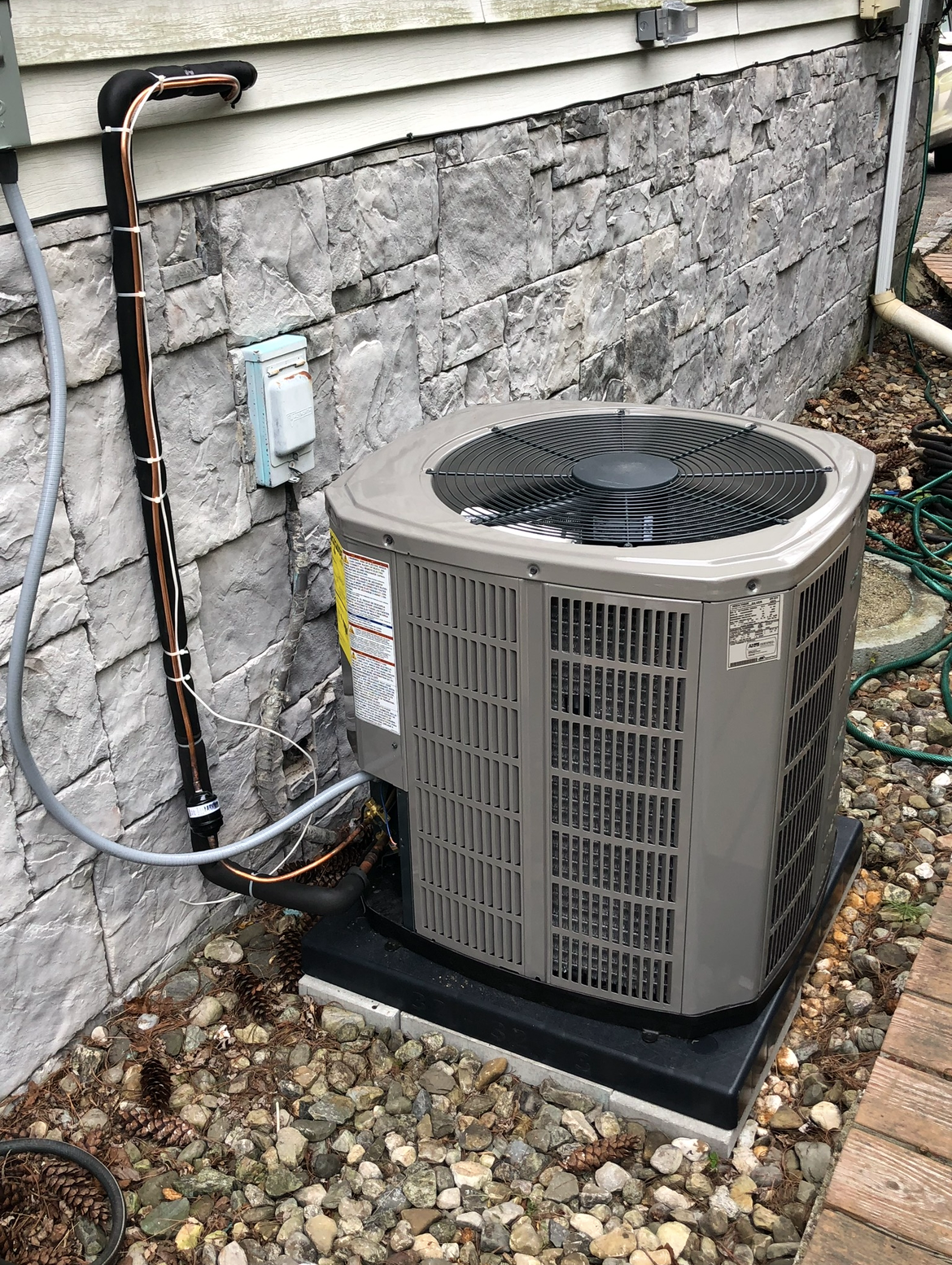 An air conditioner is sitting outside of a house next to a brick wall.