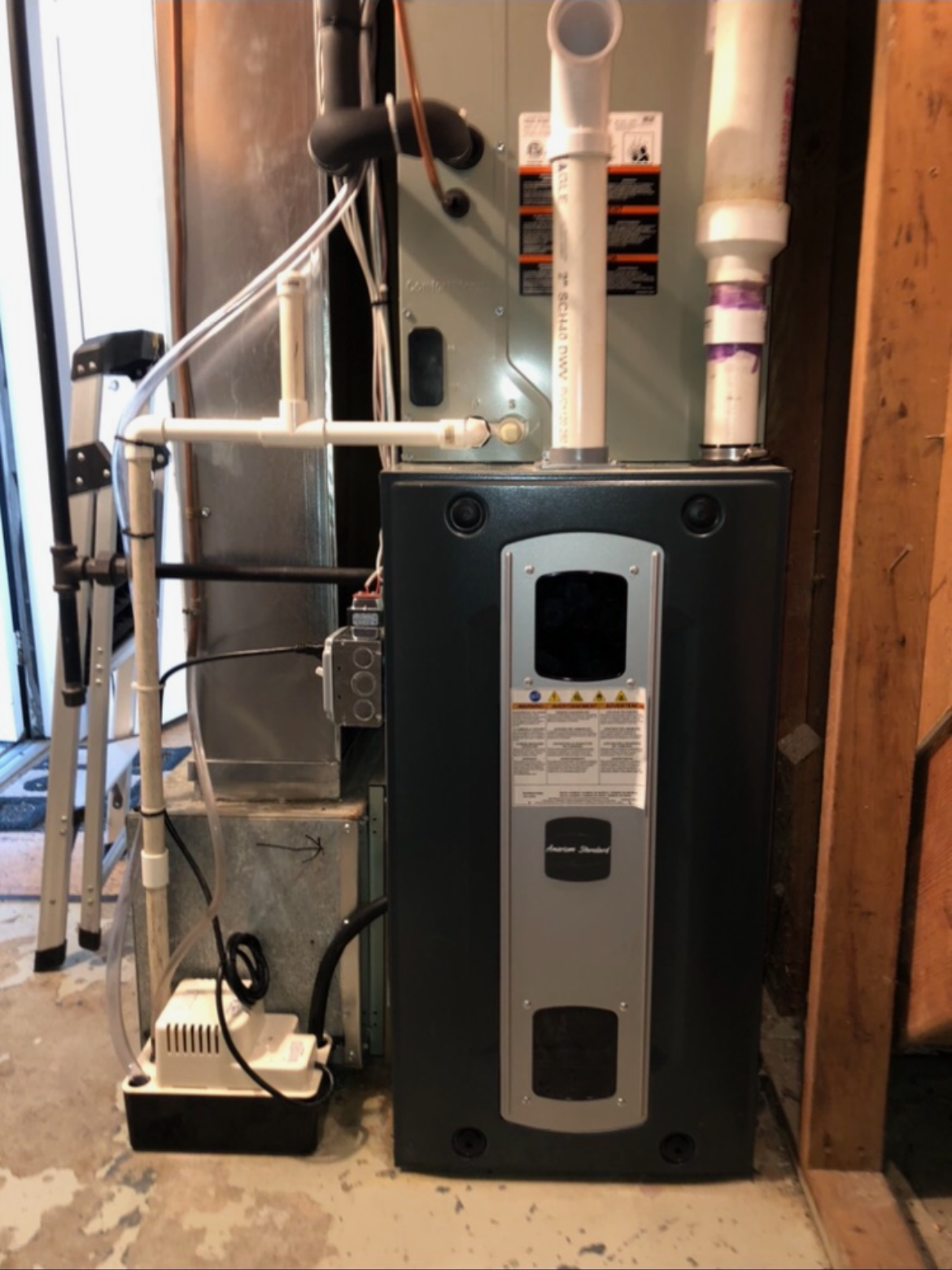 An air conditioner is sitting in a basement next to a ladder.