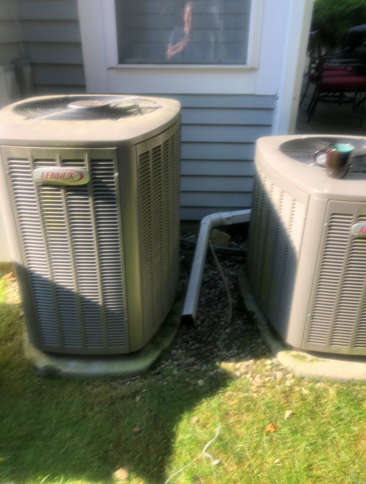 Two air conditioners are sitting next to each other on the side of a house.