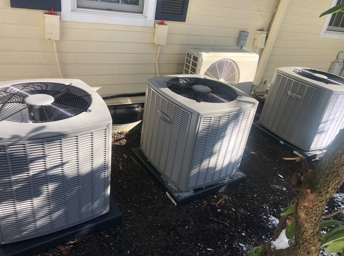 Three air conditioners are sitting on the ground outside of a house.