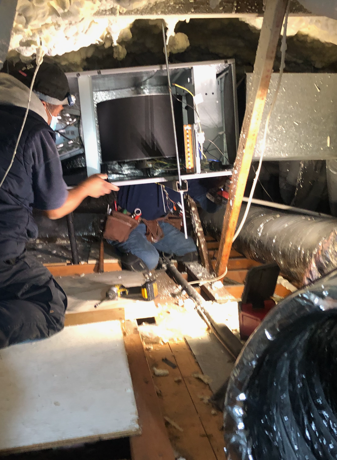 A man is working on an air conditioner in an attic.