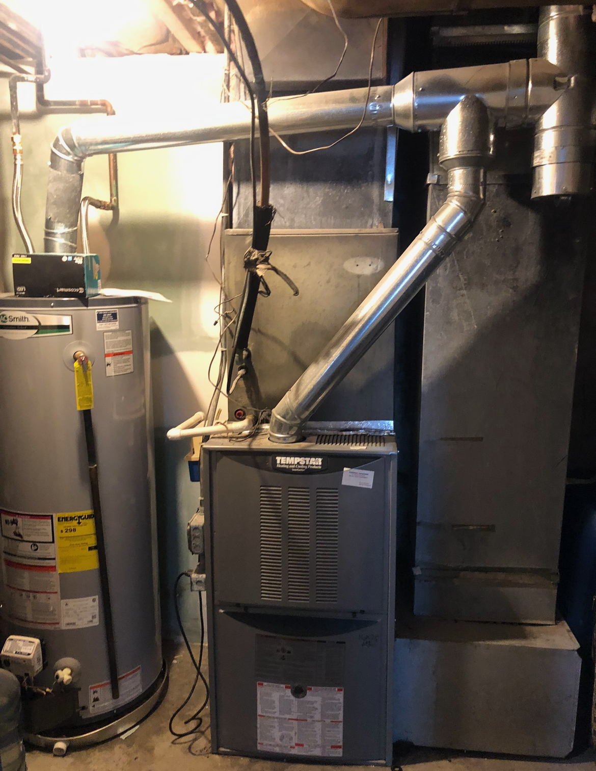 A furnace is sitting in a basement next to a water heater.