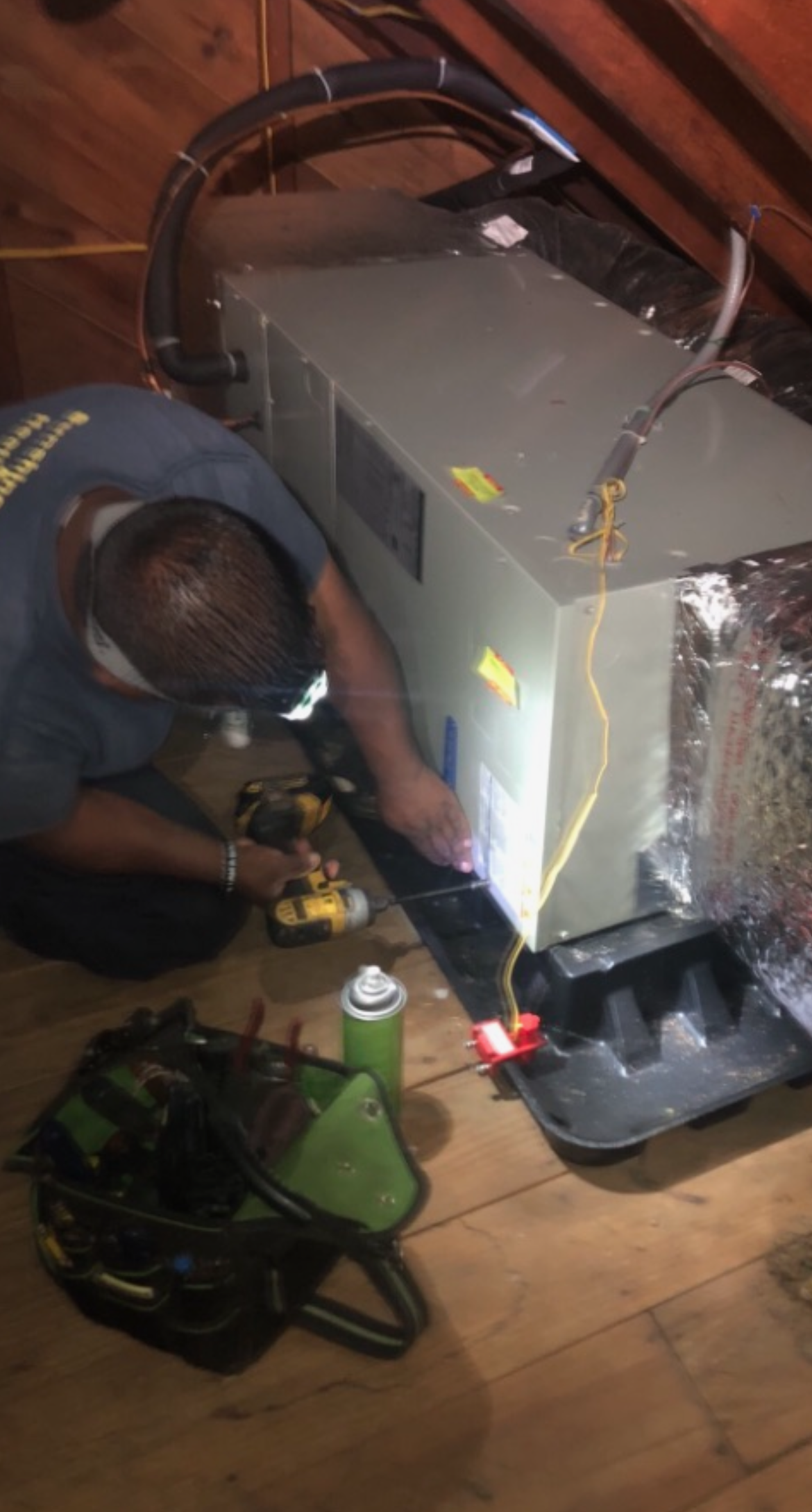 A man is laying on the floor working on an air conditioner.