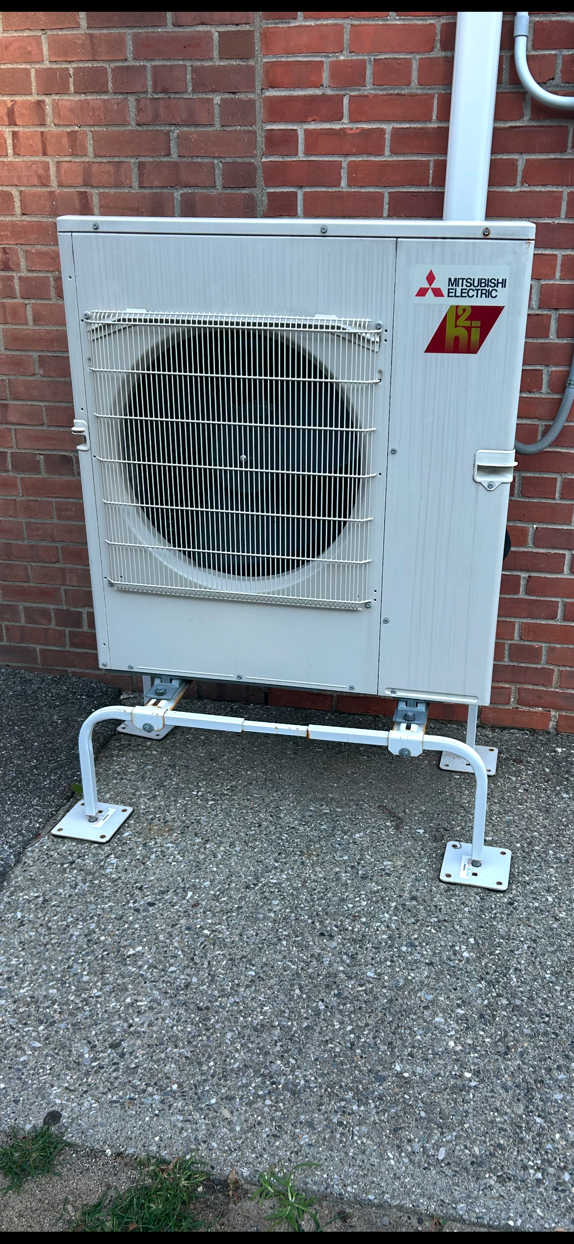 A white air conditioner is sitting on the side of a brick building.