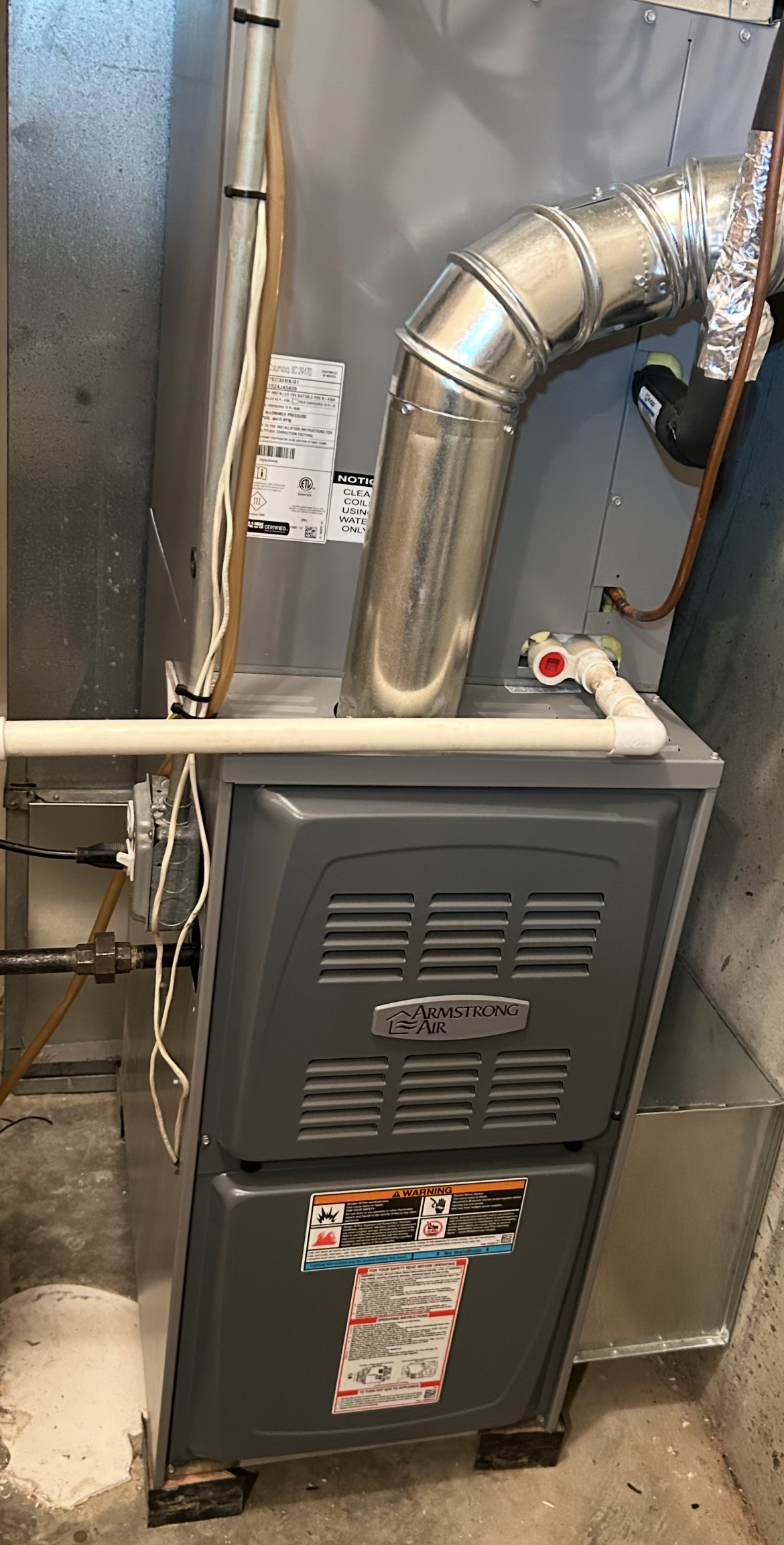 A furnace is sitting in a basement next to a pipe.