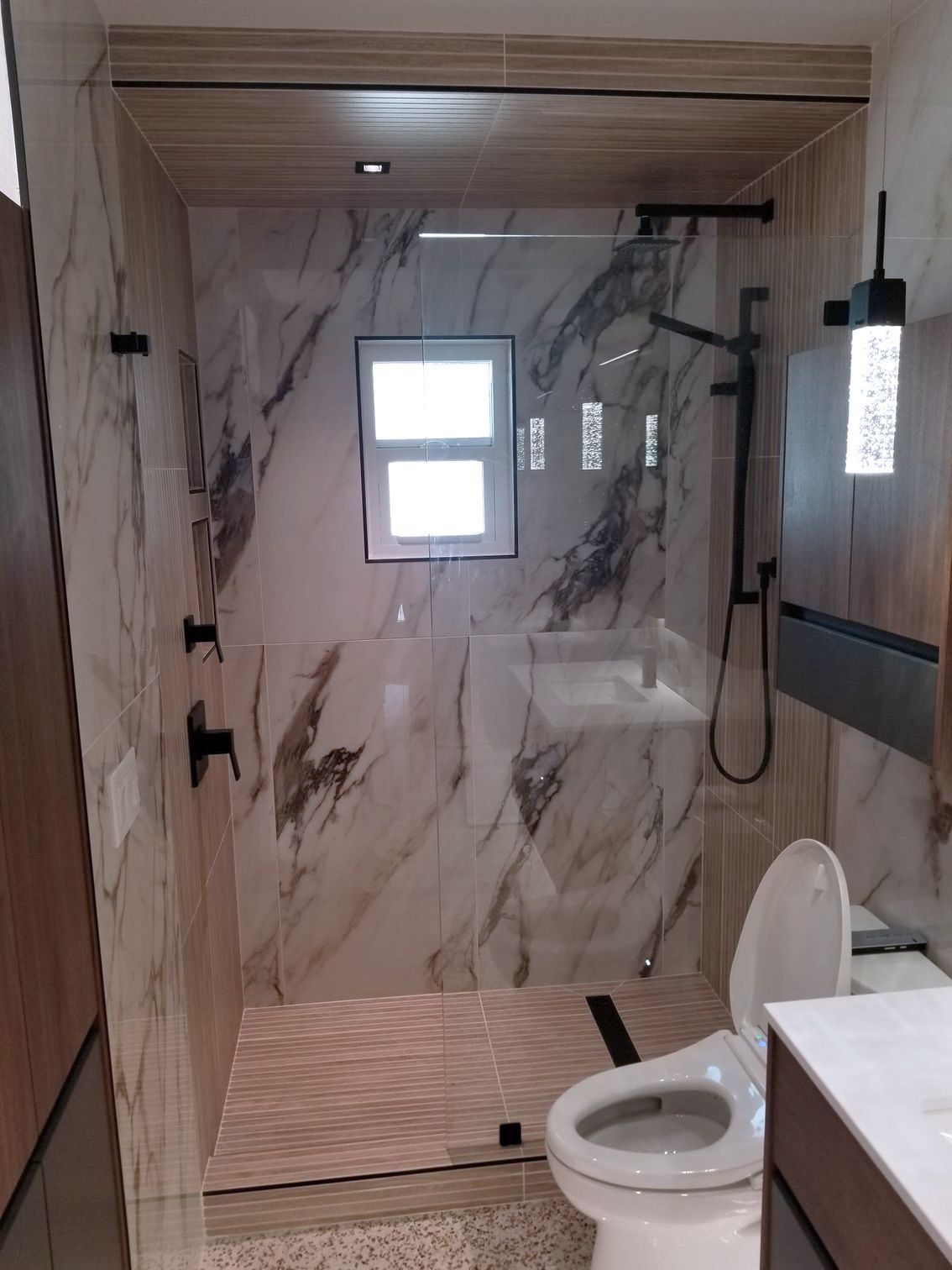 A bathroom with a toilet, shower, and marble walls