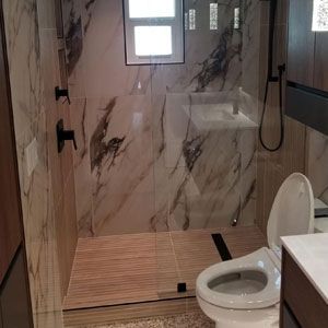 A bathroom with a toilet, sink, shower, and marble walls
