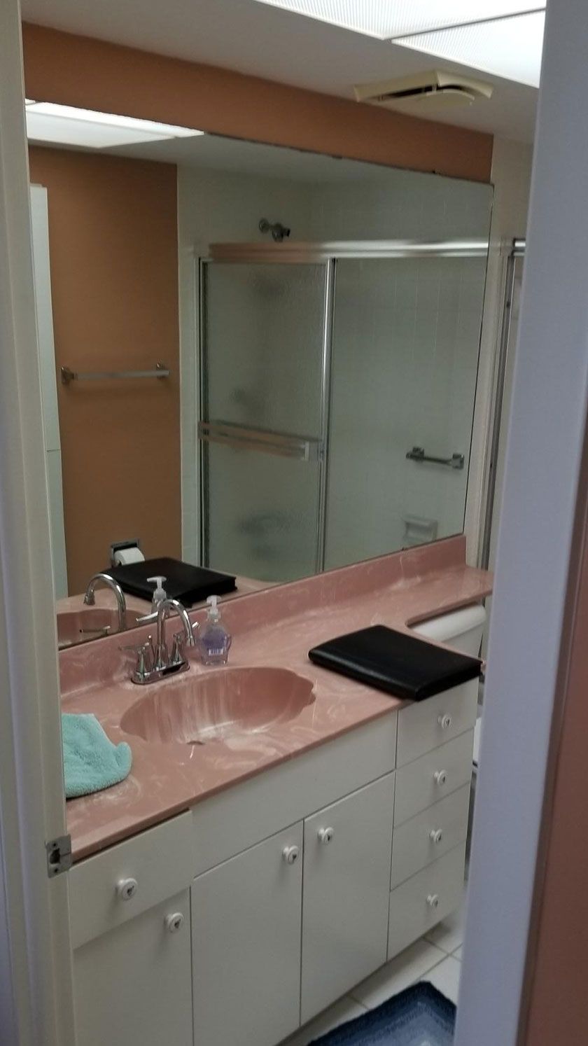 Bathroom with a pink countertop, white cabinets, large mirror, and a shower with a sliding glass door