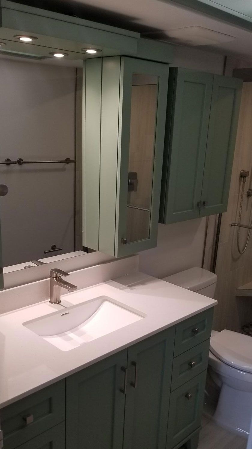 Bathroom with sage green cabinets, white countertop and sink, mirror, and toilet