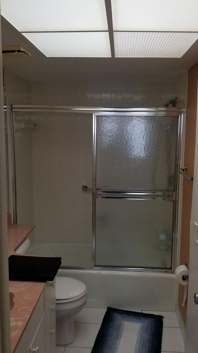 Bathroom with white tile, a bathtub with a sliding glass door, toilet, and a small rug