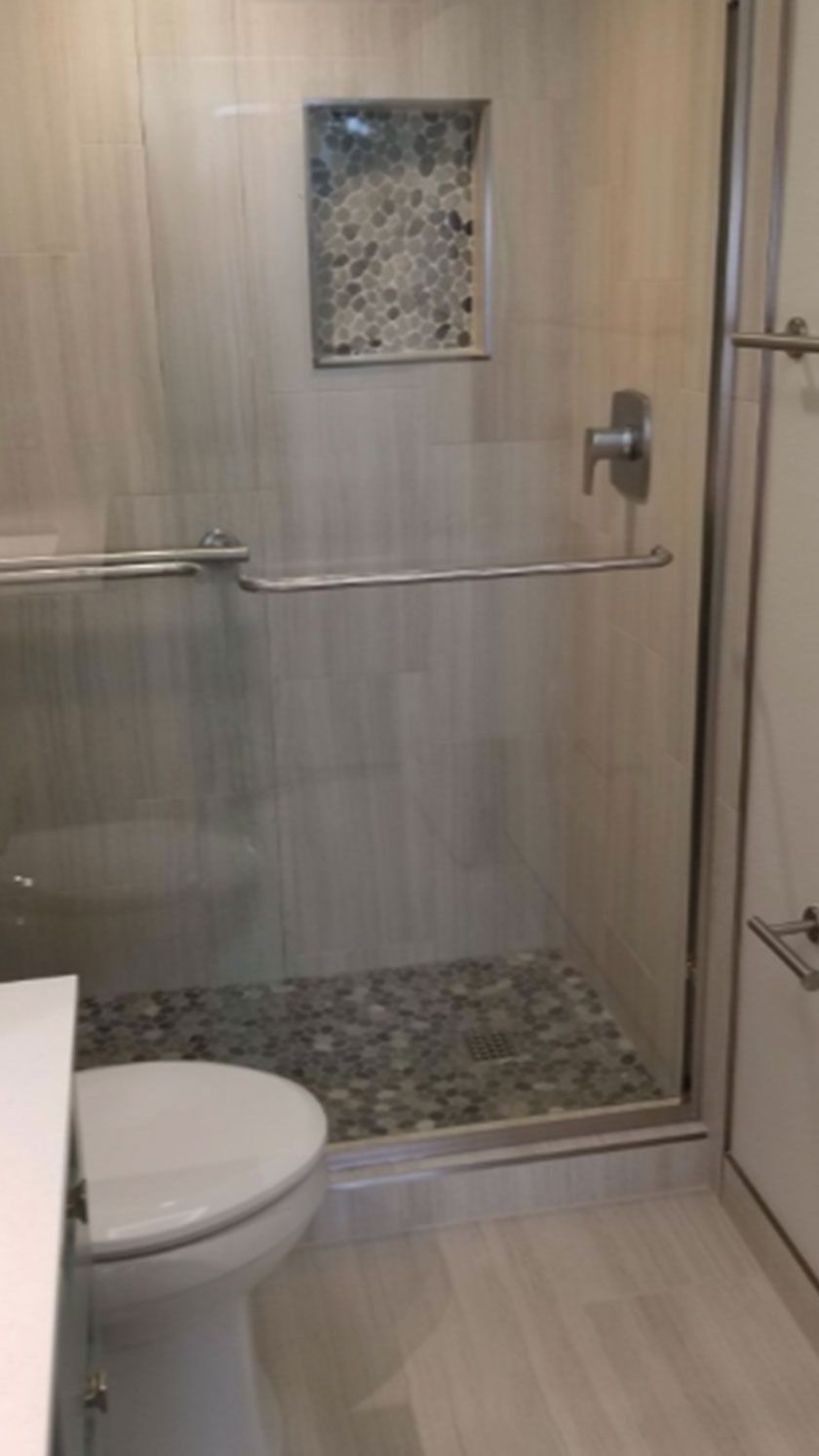 Bathroom with glass shower door, pebble floor, built-in shelf, and toilet