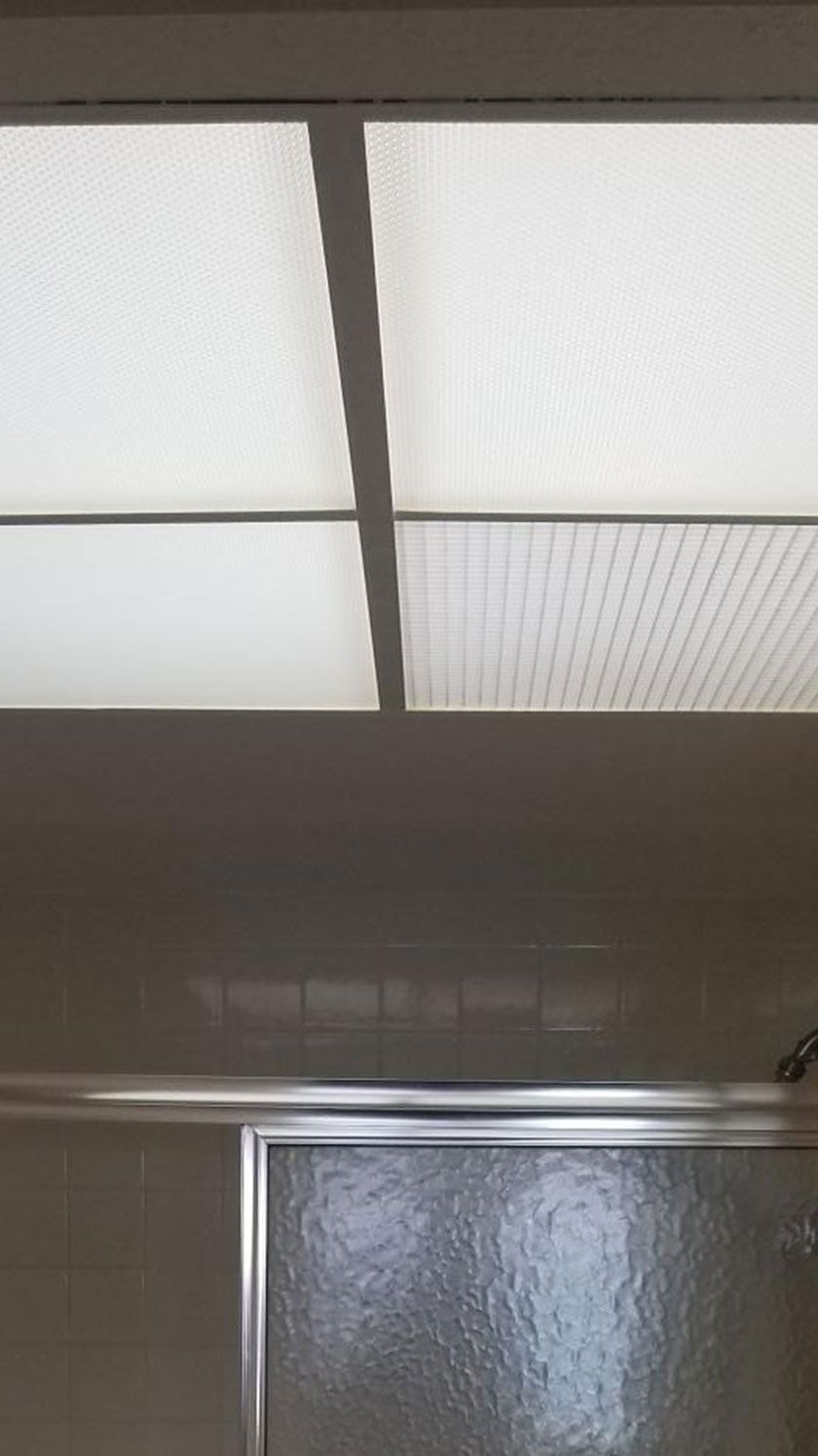 Overhead view of a bathroom shower with a frosted glass door and a rectangular, lit ceiling panel