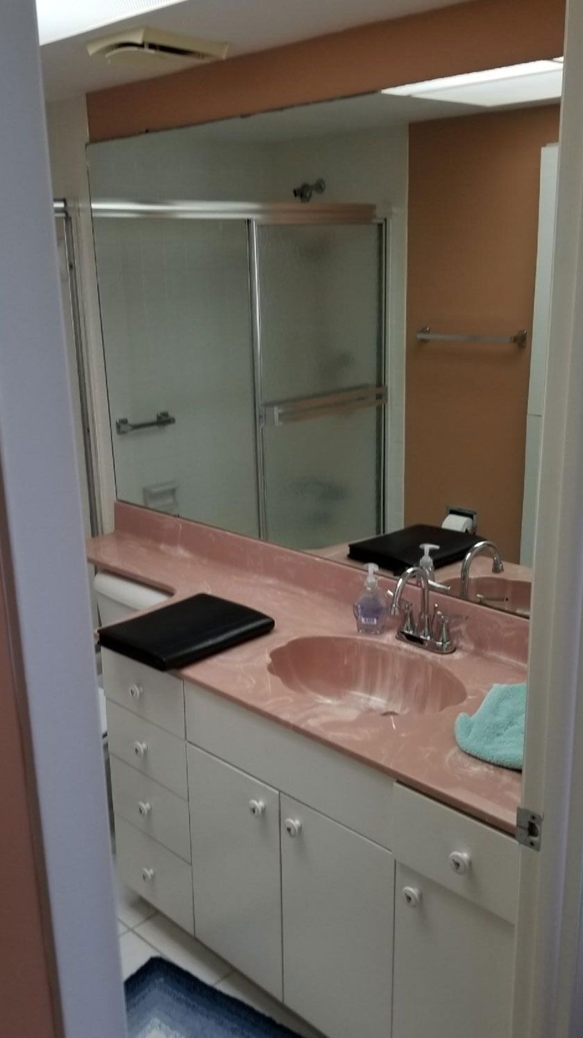 Bathroom with pink countertop, white cabinets, and a large mirror reflecting a shower