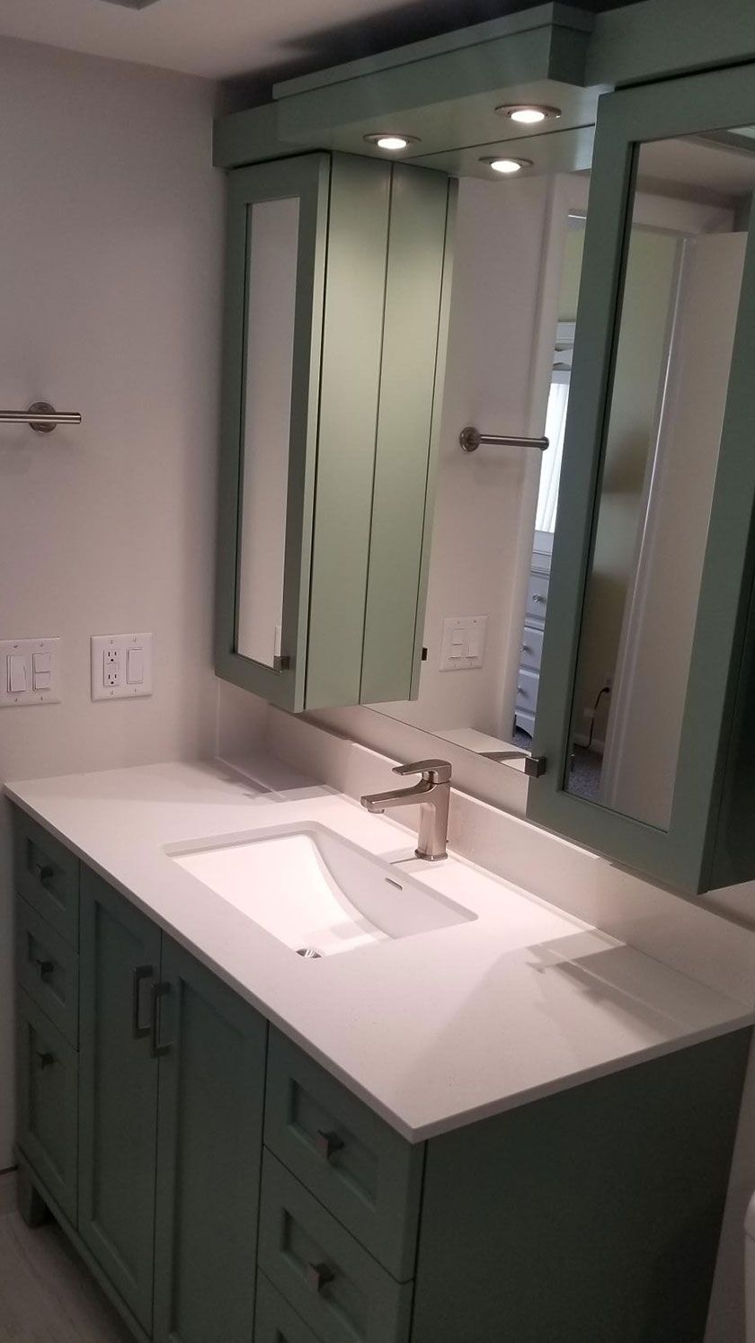 Bathroom vanity with light green cabinets, white countertop, and large mirrored medicine cabinet