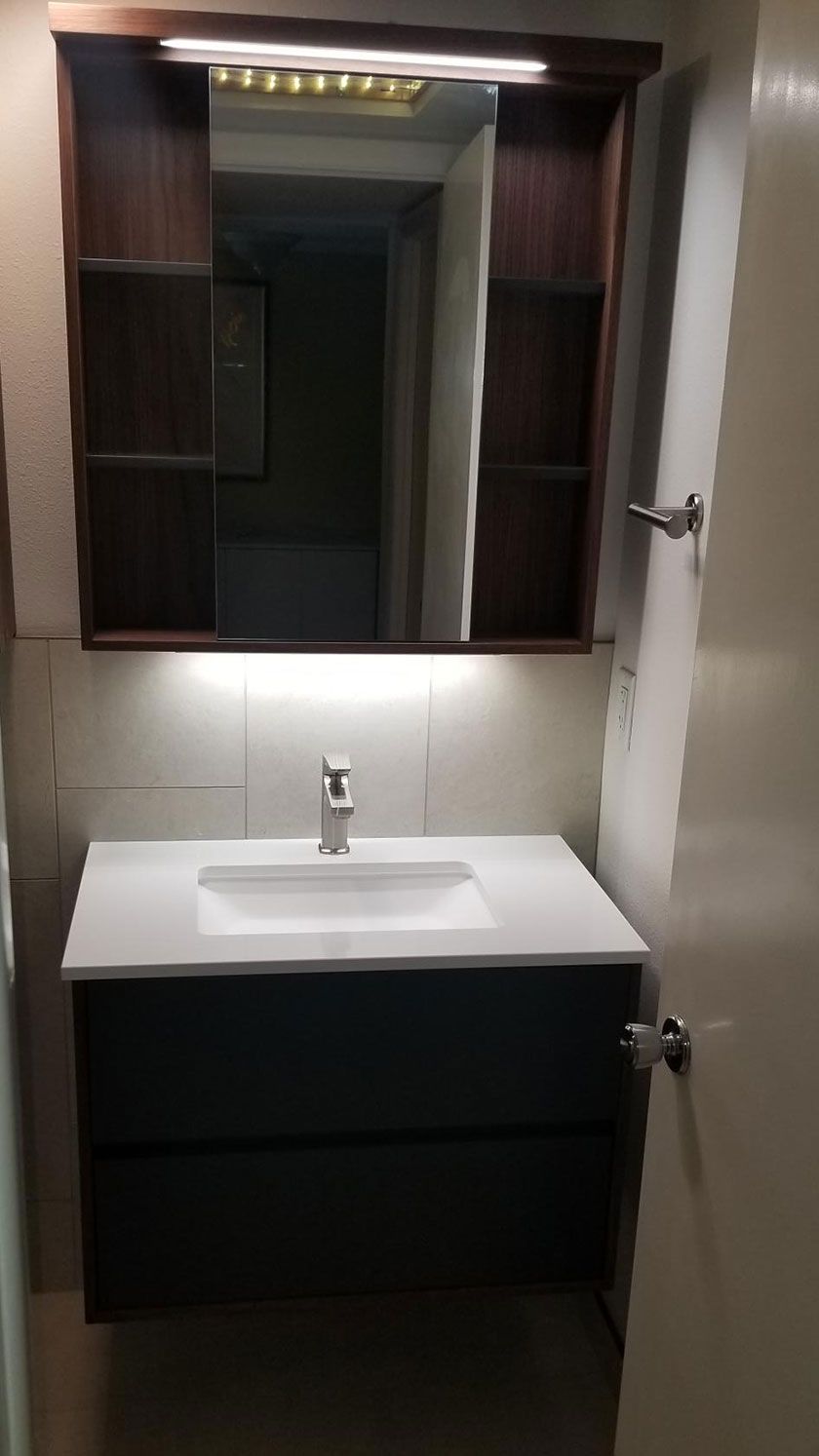Modern bathroom with dark blue vanity, white countertop, mirror, and medicine cabinet