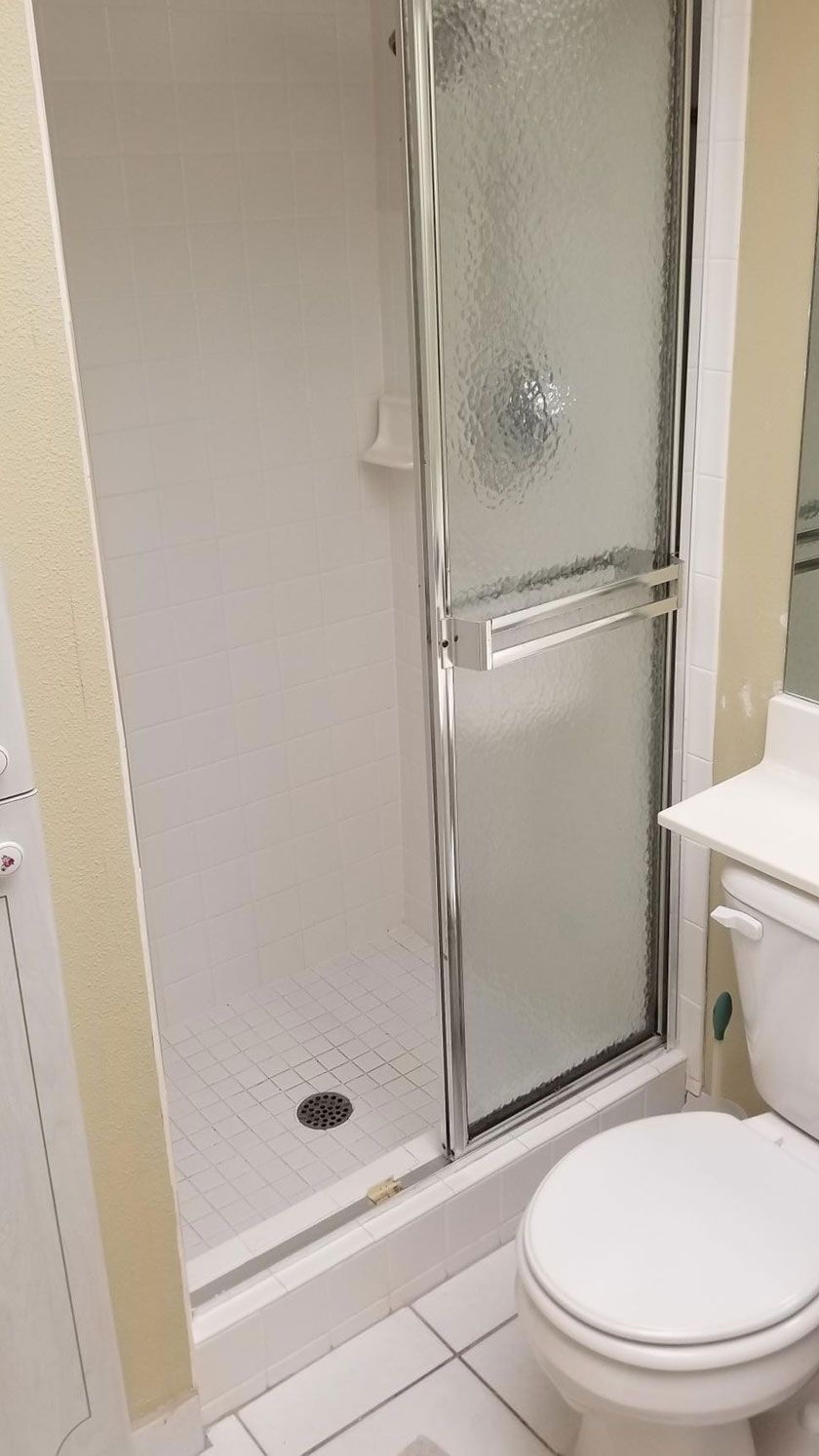 A narrow, white-walled shower with glass door and silver handle