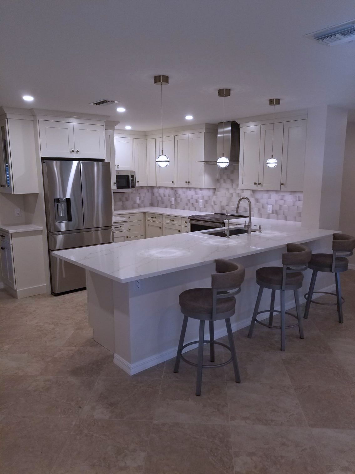 A kitchen with white cabinets, stainless steel appliances, and stool chairs
