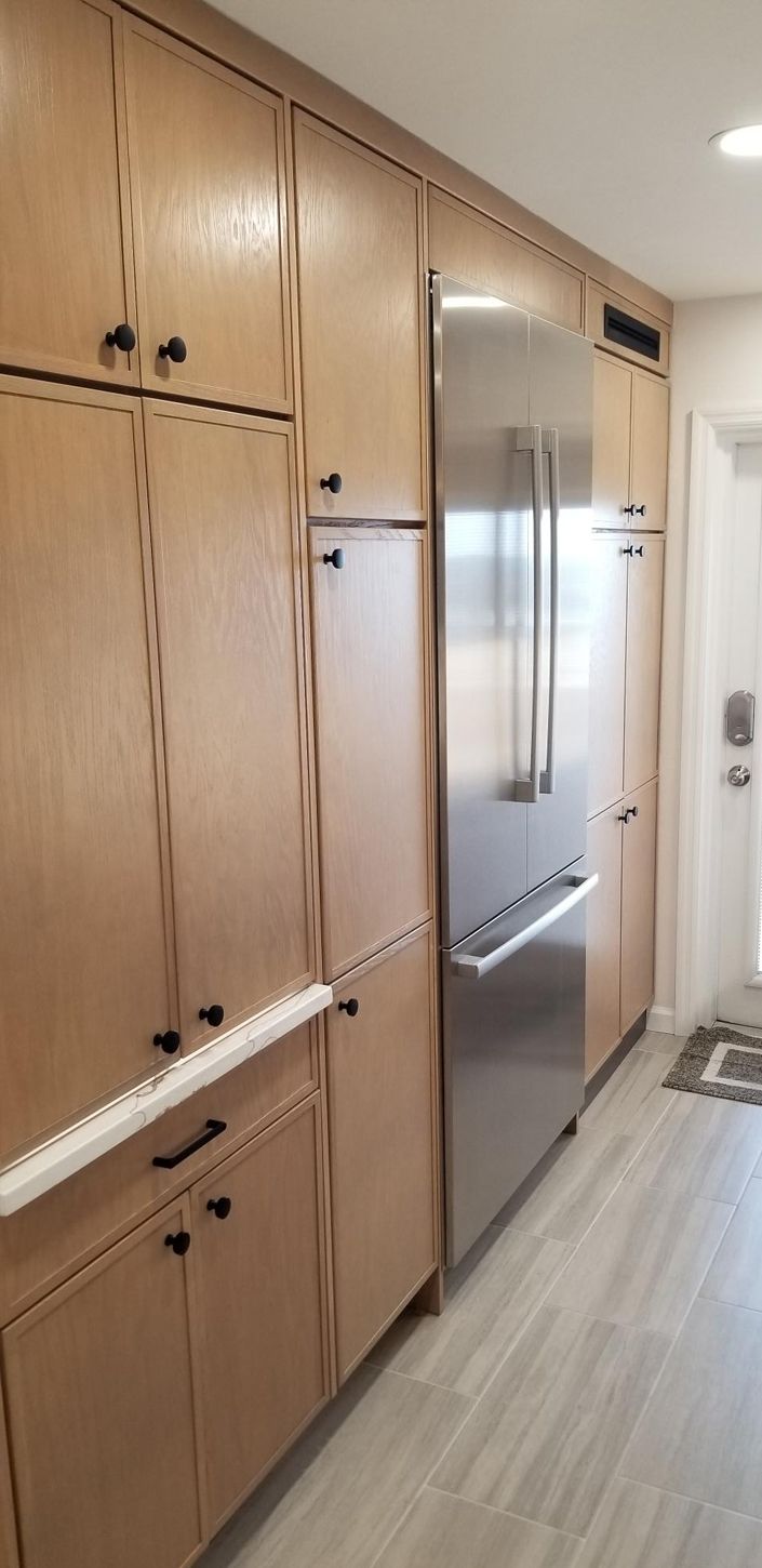 Modern kitchen with light wood cabinets and black handles. A sleek stainless steel refrigerator is integrated into the cabinetry, creating a clean, cohesive look.