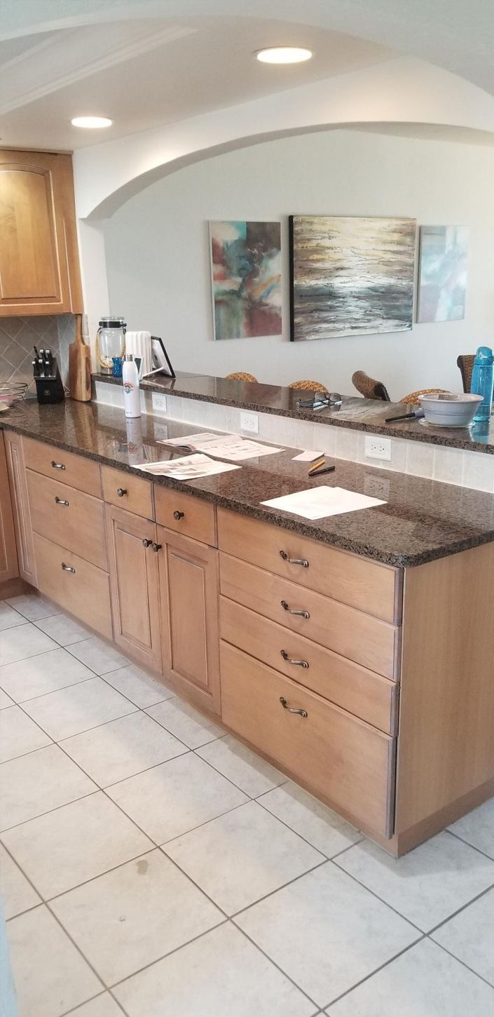 Bright kitchen with wooden cabinets and granite countertops. Papers and a blue water bottle are on the counter. Art decorates the light-colored walls.
