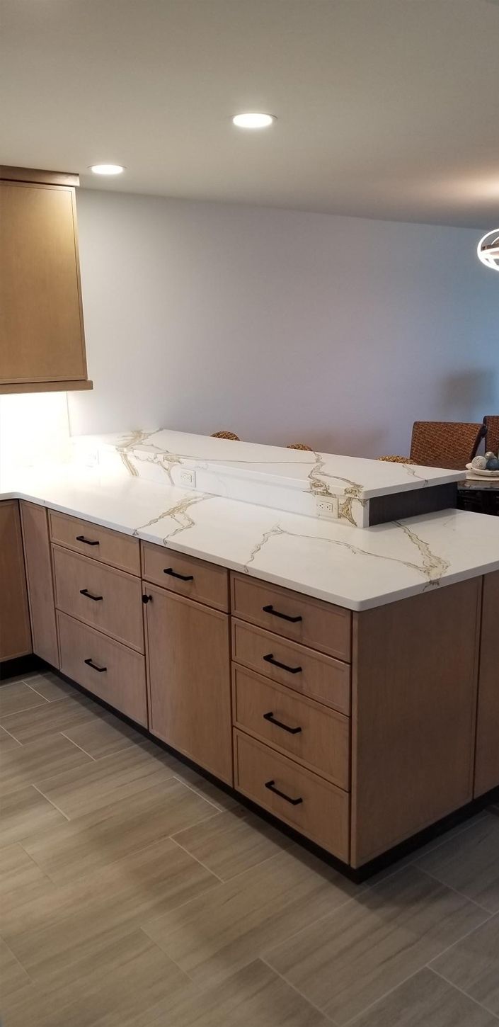 Modern kitchen with wooden cabinets and a white marble countertop, featuring subtle gold veining. The room has a cozy, minimalist feel.