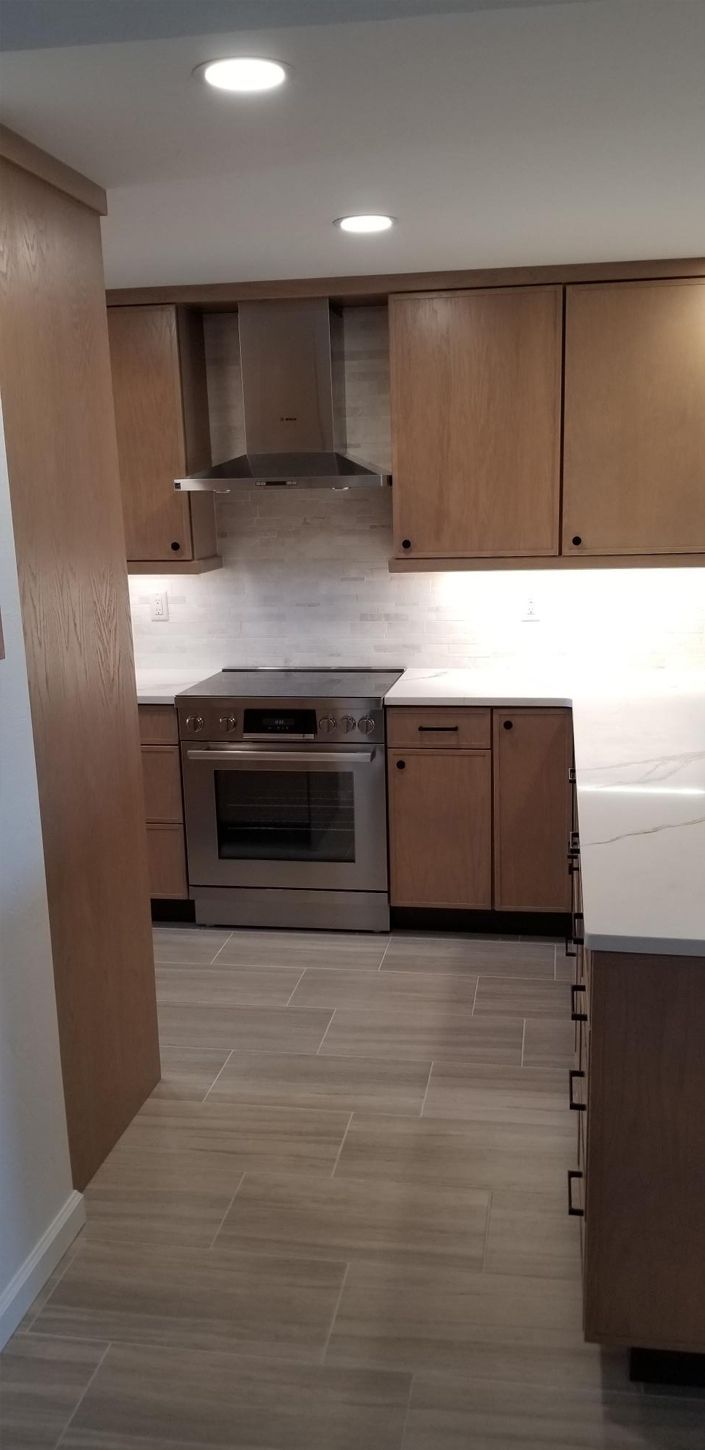 A kitchen featuring light wooden cabinets, stainless steel appliances, and light-colored tile flooring.