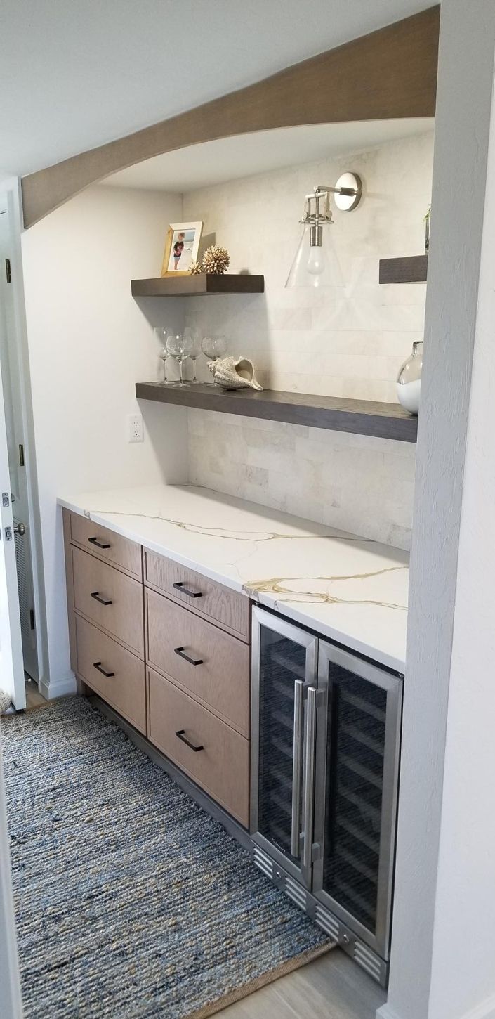 Sleek home bar with wooden shelves displaying decor, glasses, and a light fixture.