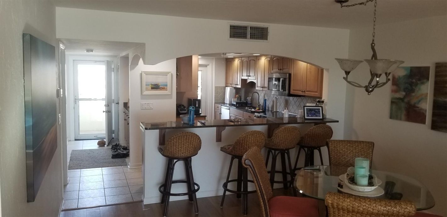 A cozy kitchen with a bar counter and four wicker stools. Stainless steel appliances and wooden cabinets are visible.