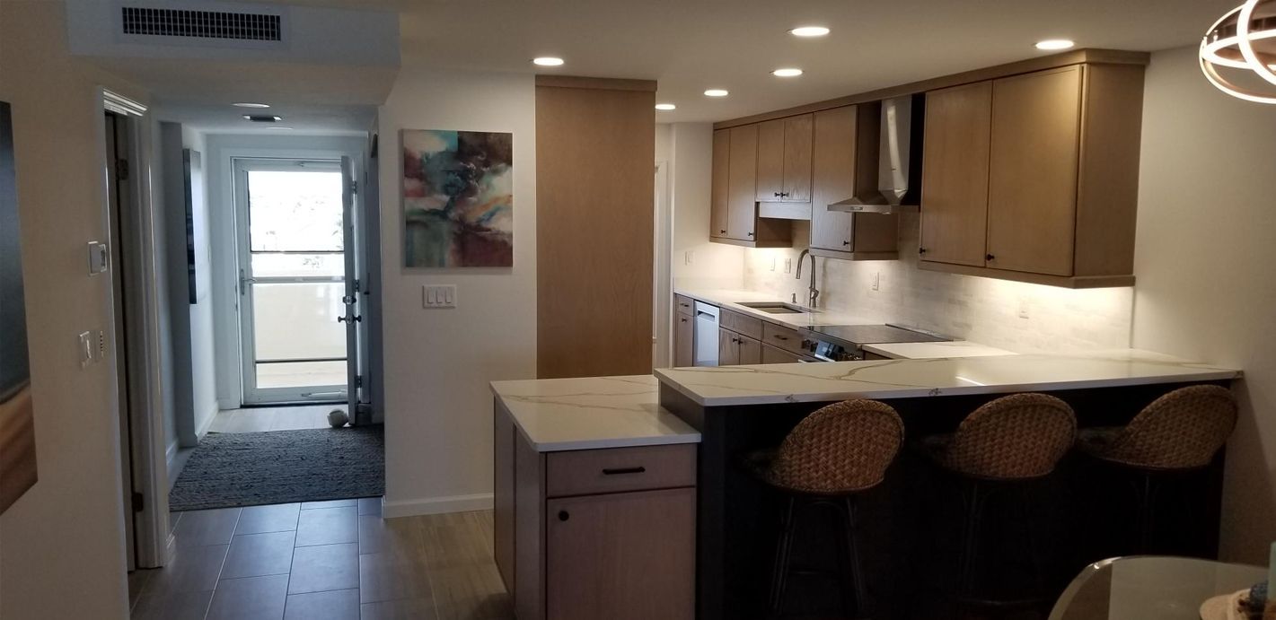 Modern kitchen with light wooden cabinets and marble countertops. Three wicker bar stools line an island. Bright, inviting ambiance.