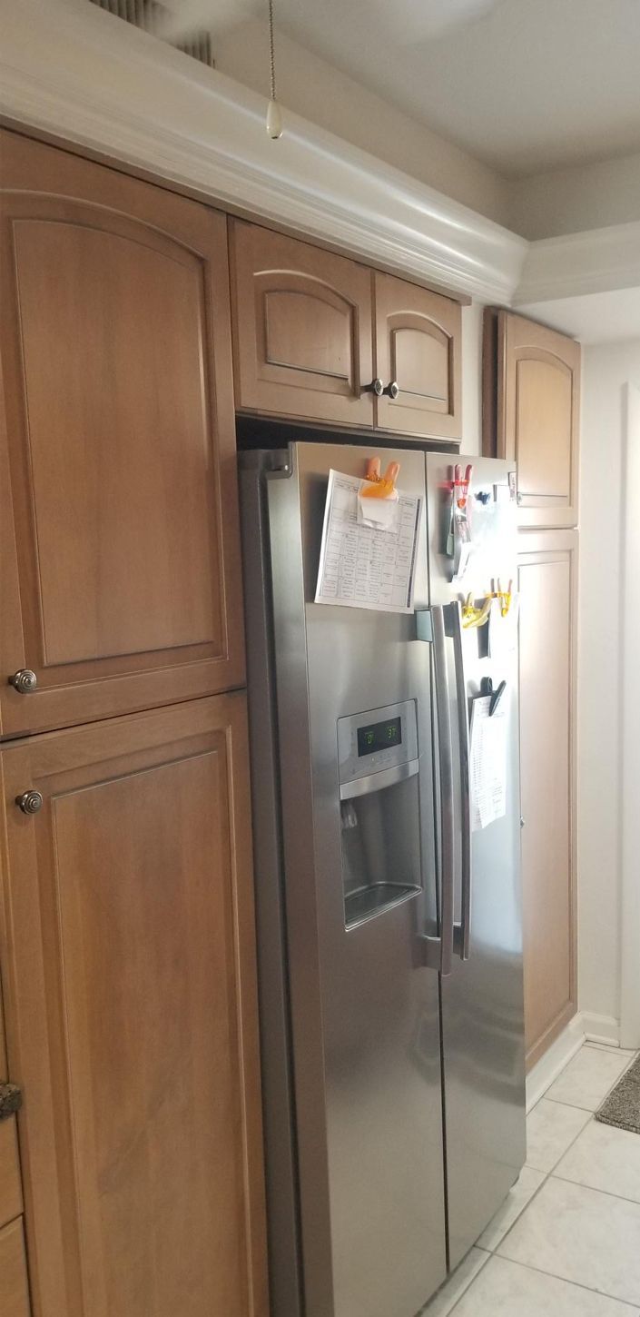 A kitchen features wooden cabinets and a stainless steel refrigerator adorned with clipped papers. The scene is bright, orderly, and functional.