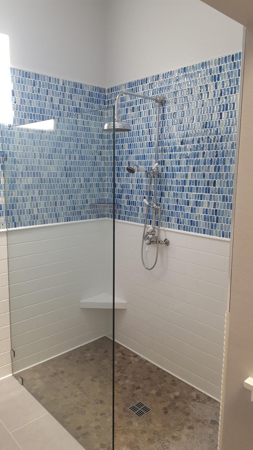 A walk in shower with blue and white tiles and a glass door