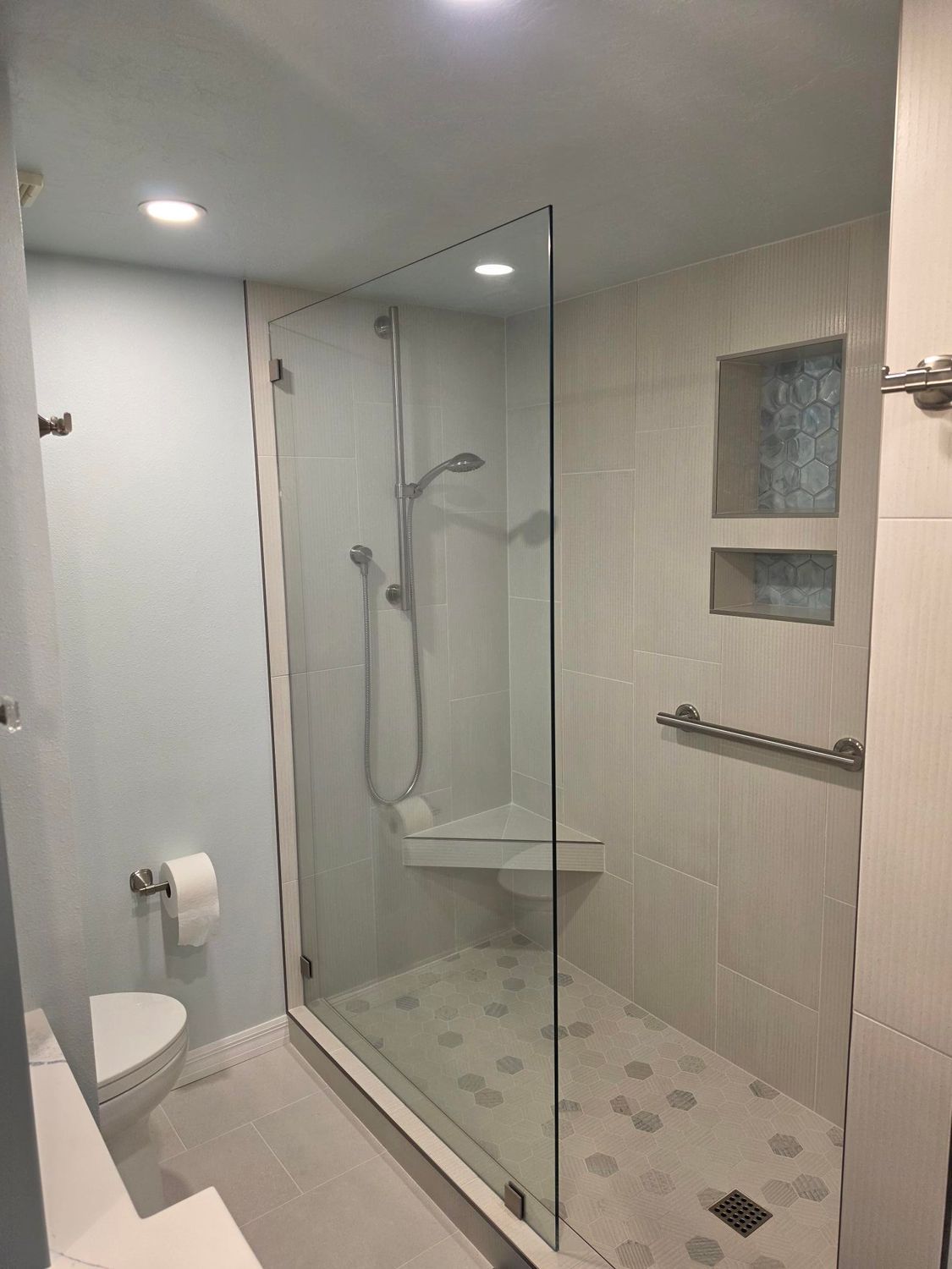 Modern bathroom with glass-enclosed shower, toilet, and built-in wall shelves