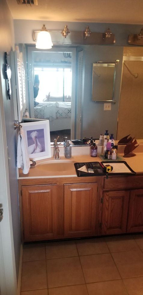 Bathroom vanity with mirror, wooden cabinets, tiled floor, and countertop toiletries